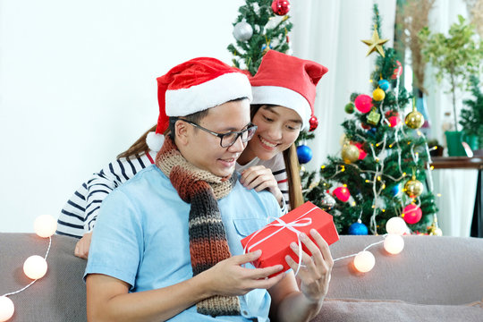 Young asian couple giving red Christmas gift box at Christmas celebate party at home, Christmas couple concept