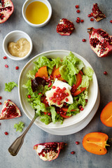 Seasonal salad with persimmon, pomegranate and dressing from honey and mustard. Wooden background, top view
