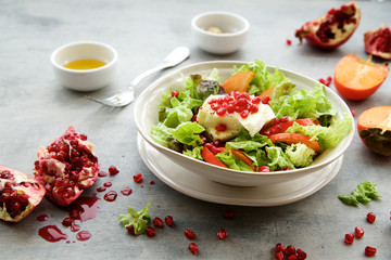 Seasonal salad with persimmon, pomegranate and dressing from honey and mustard 
