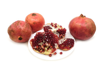 Whole and half pomegranates with ripe seeds on plate isolated on white background front view closeup
