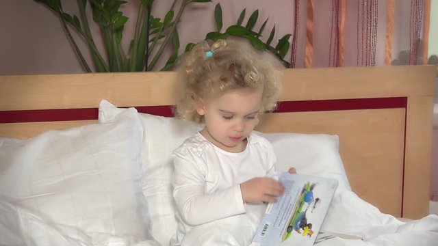 Little cute girl turn book pages sitting in bed