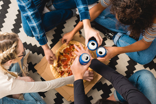 cropped image of teens clinking with cans and taking pizza