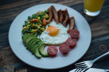 English breakfast. Fried eggs, sausages, avocado, beans, toasts, tomatoes, orange juice on wooden table. Top view with copy spac