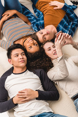 overhead view of multiethnic friends lying on bed and looking at smartphone