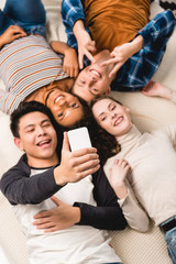 overhead view of multiethnic teens taking selfie while lying on bed