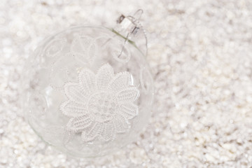 Obraz na płótnie Canvas New Year's transparent ball on a blurry background with a bokeh. Glass ball with white lace. Christmas decorations. Copy space. Selective focus.