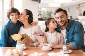 Dad and the little son are giving flowers to mother and daughter in a cafe.