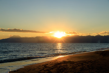 Junger, sexy Mann läuft, spaziert barfuß am Strand durchs Wasser in den Sonnenuntergang. Hält...