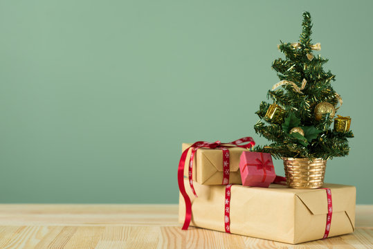 Christmas background. A small Christmas tree and boxes with gifts on a wooden table. Green background. Space for text. New Year's background.