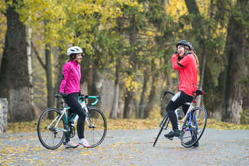Two Young Smiling Female Cyclists with Road Bicycles Resting and in Park in Cold Autumn Day. Healthy Lifestyle.