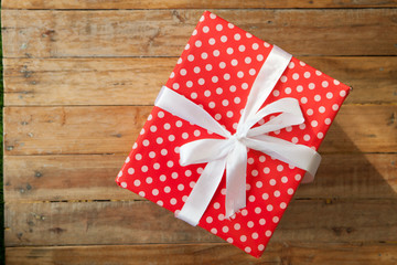 Obraz premium Red gift box and red ribbon and mini heart inside on wood background with space..