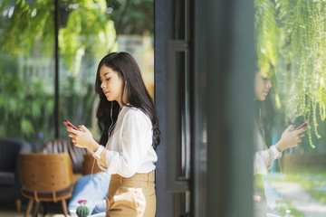 Happy young asian woman with long hair using and listening music on smartphone in cafe