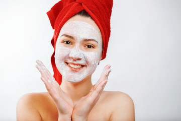 happy beautiful girl with a red towel on her head applies a scrub on the face of a large portrait on a white background