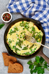Frittata with asparagus and green peas in a frying pan on a concrete background.