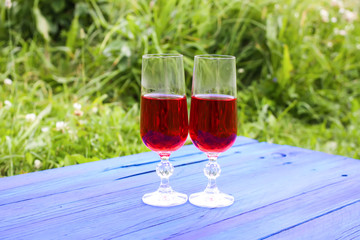 Two glasses with homemade red wine on blue boards outdoors in a countryside at summer.