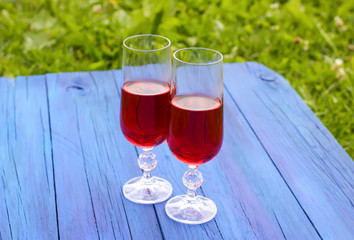 Two glasses with homemade red wine on blue boards outdoors in a countryside at summer.