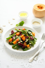 Fresh autumn salad with marinated pumpkin and beetroot, spinach leaves,olive oil, sesame and pumpkin seeds on white table cloth. Space for copy