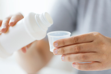 woman pouring syrup from bottle to medicine cup