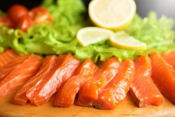 pieces of red fish with lemon and cherry tomatoes on a wooden board