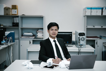 Asian handsome Businessman in suit work hard with crumped paper in the office,Young man stressed about the declining sales of the company,dark tone,thailand people