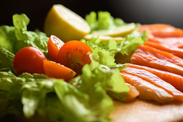 pieces of red fish with lemon and cherry tomatoes on a wooden board on a black background