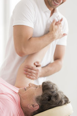 Physiotherapist stretching senior woman's shoulder - obrazy, fototapety, plakaty