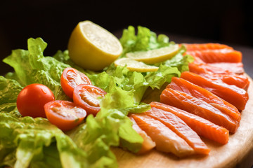 pieces of red fish with lemon and cherry tomatoes on a wooden board on a black background