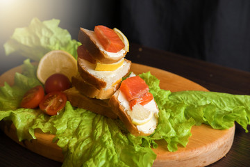 sandwich with red fish lemon tomatoes and salad on a wooden board on a black background
