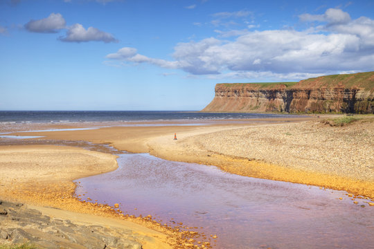 The beach at Saltburn-by-the-Sea and Huntcliff. There is a stream running across the beach, and also a traffic cone in the middle of the picture.