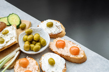 Top view of a crusty baguette slices with cherry tomatoes, cucumbers and green olives, cream cheese.