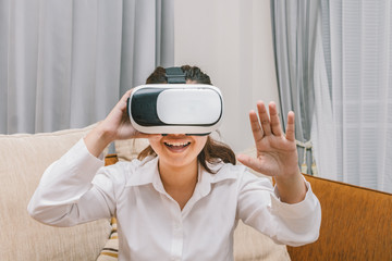 Asian woman playing virtual reality glasses  on brown sofa, smartphone using with VR glasses
