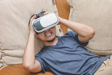 A man wearing and playing virtual reality enjoying in scared content on brown sofa, Innovation technology