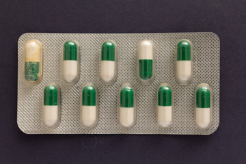 Expired white and green capsules in medicine box. Pills over black background.