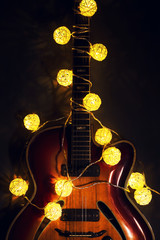 Old electric guitar with a lighted garland on a dark background. Greeting, Christmas, New Year greeting card. Copy space.