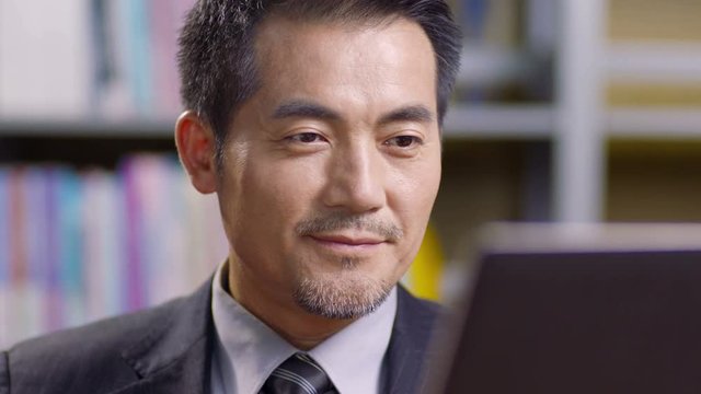 asian businessman drinking coffee while working in office using laptop computer. 