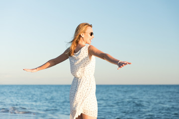 Junge Frau tanzt glücklich am Strand in der Sommersonne. Sie trägt ein weisses kurzes Sommerkleid...