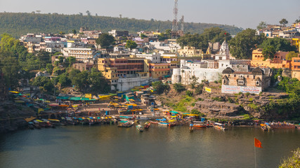 Omkareshwar cityscape, India, sacred hindu temple. Holy Narmada River, boats floating. Travel destination for tourists and pilgrims.