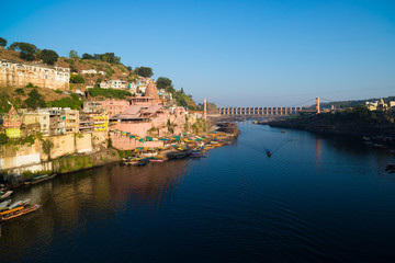 Fototapeta premium Omkareshwar cityscape, India, sacred hindu temple. Holy Narmada River, boats floating. Travel destination for tourists and pilgrims.