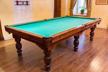 Large wooden table with green cloth for playing billiards
