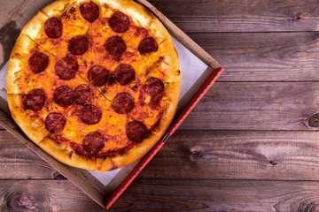 Pizza with salami in a box on a wooden background with copy space. Top view.