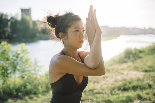 Young Japanese woman practicing yoga exercises near a river in a summer day in the city