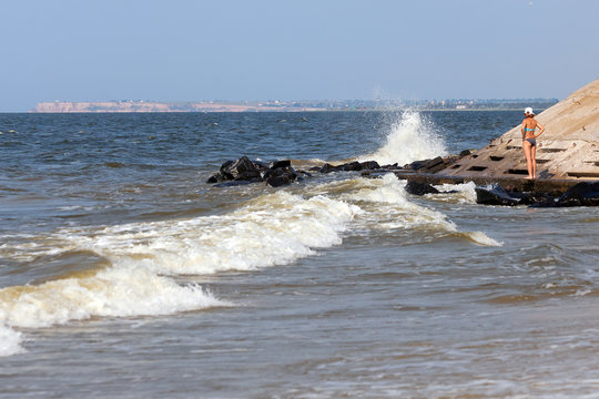 Lonely young woman stand in deserted beach alone. Early morning. The sea after the storm with dirty wate