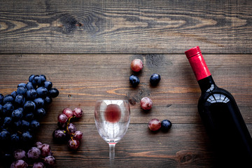 Taste red wine. Bottle of red wine, glass and black grape on dark wooden background top view copyspace