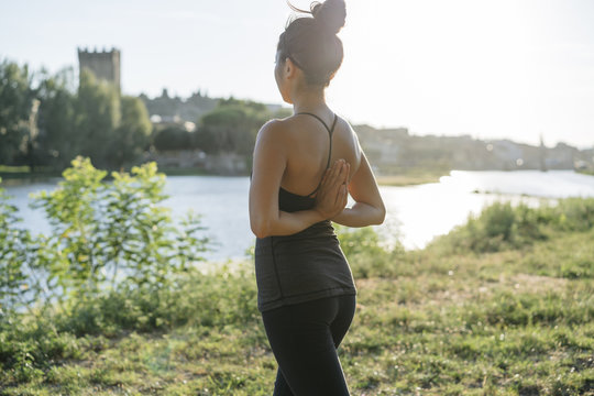 Young Japanese woman practicing yoga exercises near a river in a summer day in the city