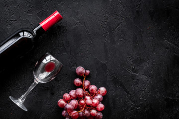 Taste red wine. Bottle of red wine, glass and red grape on black background top view copyspace