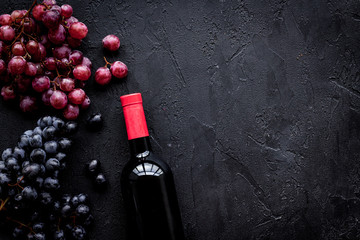 Bottle of red wine near bunch of grapes on black background top view copyspace