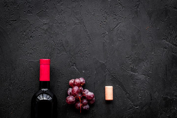 Bottle of red wine near bunch of grapes on black background top view copyspace