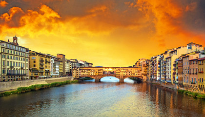 Obraz premium Beautiful city view with the famous medieval stone bridge Ponte Vecchio over the Arno river in Florence, Italy at sunset. Place of pilgrimage for tourists.