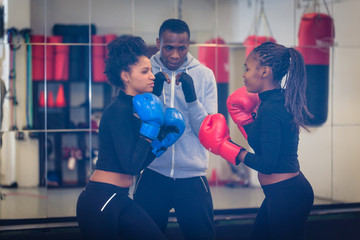 Experienced boxing trainer supervising and teaching two female boxers indoors
