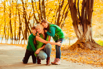Fototapeta premium Two children in green jackets hug blonde woman posing in an autumn park